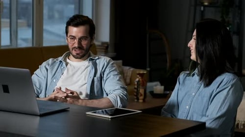 A couple of freelancers in casual wear work remotely in their home office, they use a laptop