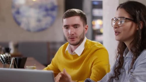 Young Coworkers Smiling and Discussing Project on Laptop in Cafe