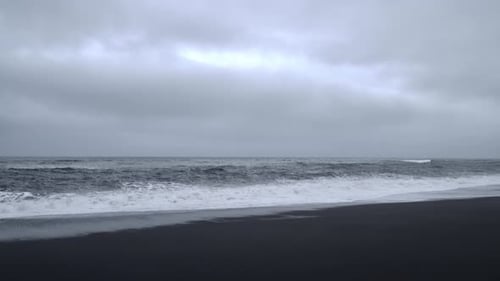 Waves Crashing on Black Sand Beach Under Cloudy Sky