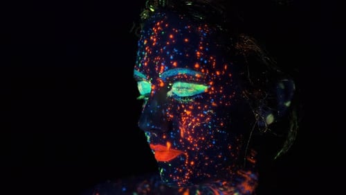 Face Painted with Glow in the Dark Paint. Fashion Model Woman in Neon Lights Posing in Studio