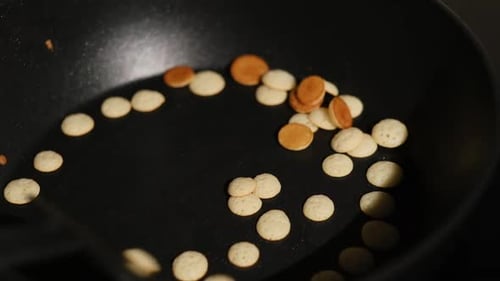 Process of cooking tiny mini pancake cereal. Dough is poured into hot pan.