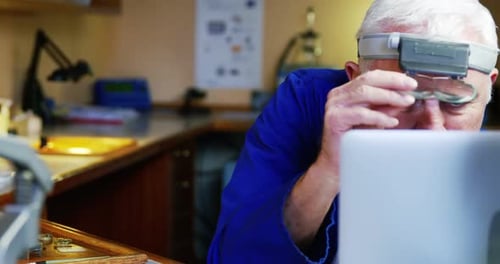 Horologist using laptop while repairing a watch