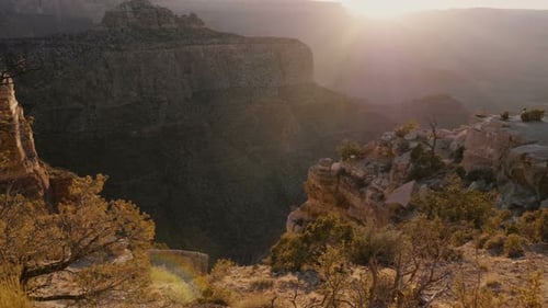 La caméra se déplace juste au-dessus des buissons sur des rochers pour révéler un panorama épique rétroéclairé au coucher du soleil