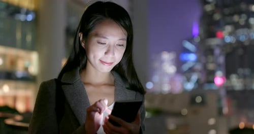 Une jeune femme d'affaires regarde un téléphone intelligent en ville la nuit