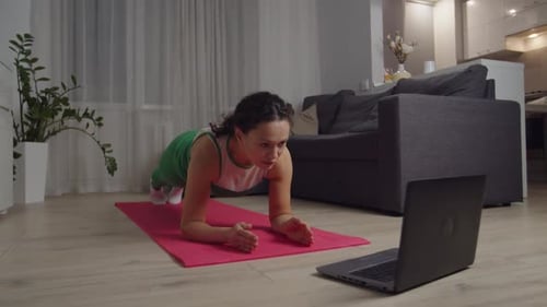 Mujer haciendo ejercicio con planchas viendo un vídeo tutorial en un ordenador portátil en interiores