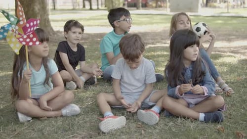 Multiethnic Kids Sitting on Grass in City Park Together