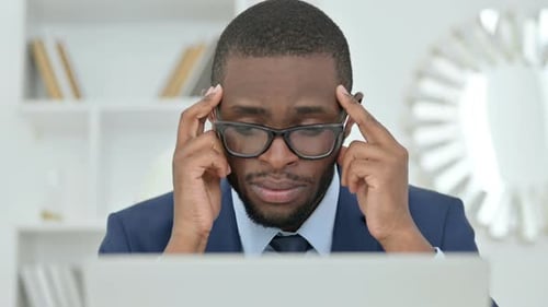 Stressed Businessman Massaging Temples in Office Environment