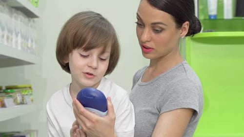 Beautiful Woman Choosing Shower Gel for Her Adorable Son at Drugstore