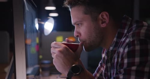 Businessman drinking coffee and working in a modern office by night