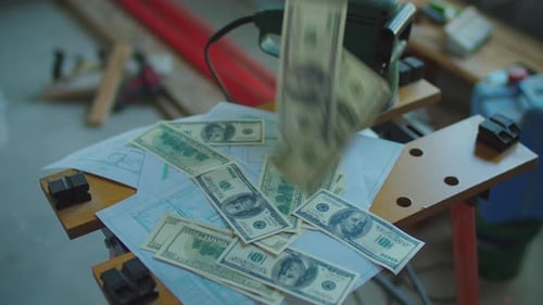 A stack of dollar banknotes flying from above on table with blueprints.