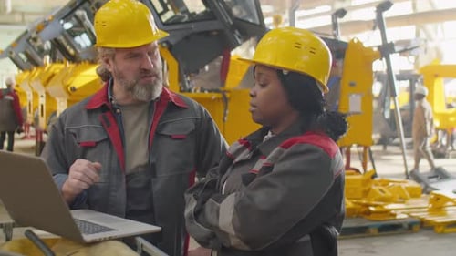 Diverse Factory Workers Using Laptop and Speaking