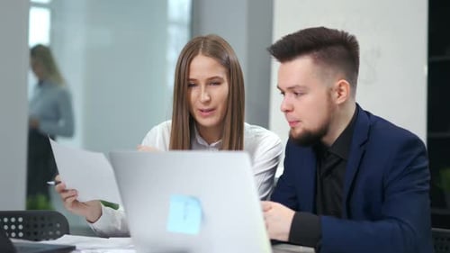 Male and Female Smiling Colleagues Discussing Working Sitting at Table in Modern Office Using Laptop