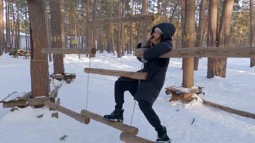 Happy Teenage Girl Climb on Swinging Suspended Wooden Logs in Winter Adventure Park in Snowy Forest