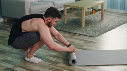 Young Man Is Rolling Up Fitness Mat and Looks at Camera