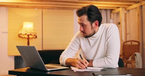 Man Working at Desk with Laptop and Writing