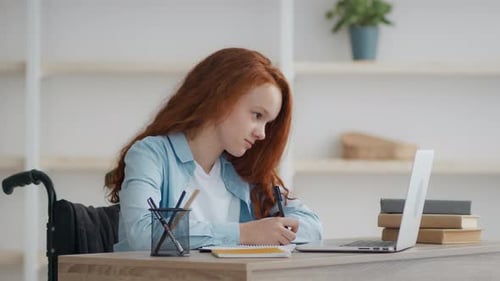Student Writing in Notebook Next to Laptop