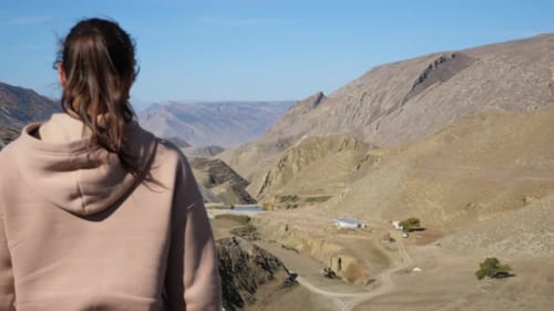 Woman in Beige and Pink Sweatshirt with a Hood Approaches a Rock in the Mountains