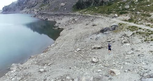 Man Running in a Rocky Off Road at the Basement of Rocky Mountain. Lake on the Mountain Coast.