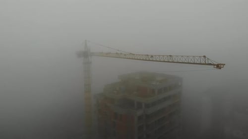 Birds eye view on tower crane in fog standing next to residential building.