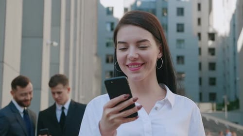 Businesswoman Smiling Using Smartphone with Colleagues Background