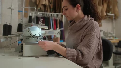 Woman Sewing Black Fabric on Machine in Workshop
