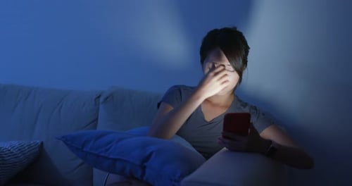 Woman Rubbing Eyes While Using Smartphone at Night