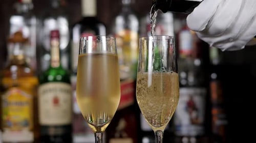 Closeup of a Waiter in Gloves Pouring Champagne Into Two Glasses at the Bar