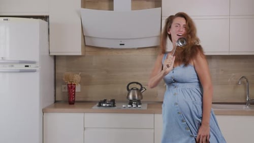 Happy Pregnant Woman Singing with Ladle in Kitchen
