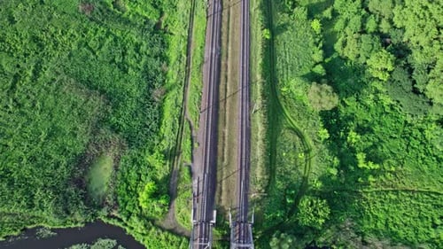 Kleiner Fluss fließt sanft zwischen grünen Feldern und einer Eisenbahnbrücke