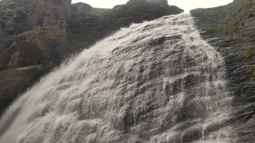 Waterfall with Foamy Water Streams Runs Down Along Rocks