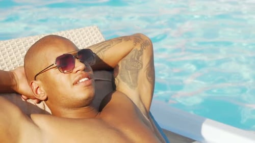 Man Lounging Poolside with Sunglasses on Sunny Day