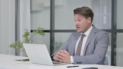 Middle Aged Man Talking on Video Call on Laptop in Office