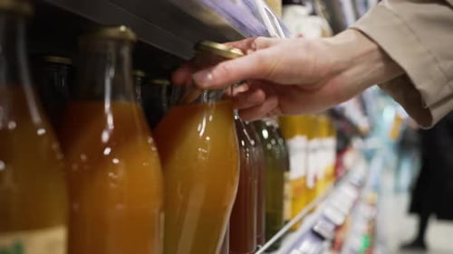 Hand Selecting Bottled Juice in Supermarket Aisle