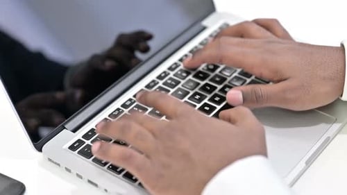 Draufsicht der Hände eines afrikanischen Mannes, der auf Laptop tippt