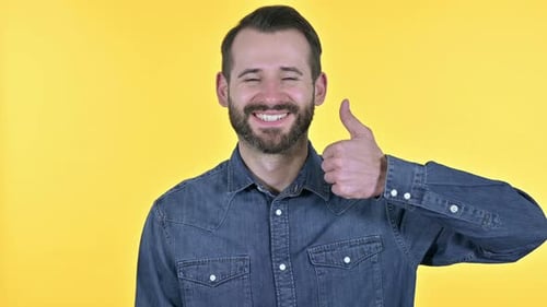Junger Mann zeigt Daumen hoch, gelber Hintergrund