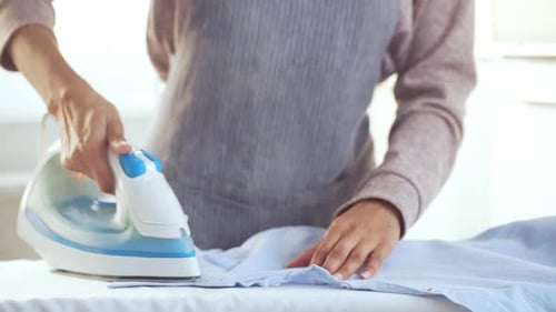 Caucasian Female's Hands Ironing Blue Shirt on White Board in Slowmotion