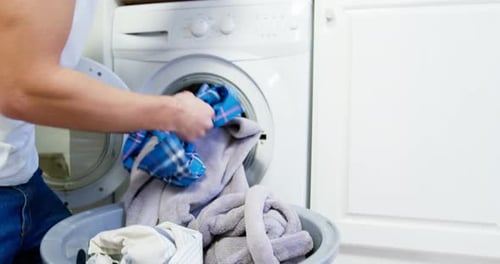 Adult Loading Clothes into Washing Machine in Laundry Room
