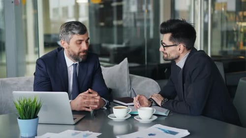 Male Coworkers Discussing Business During Lunch Break in Modern Cafe