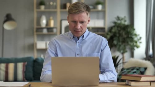 Man Working on Laptop at Desk, Frustrated