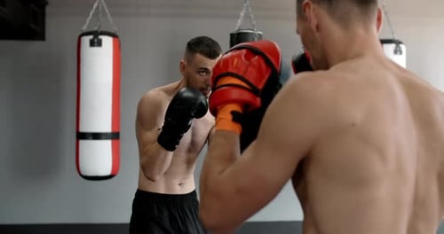 Kämpfer in Boxerhandschuhen übt seine Schläge mit Trainer in Zeitlupe im Fitnessstudio Kickboxer