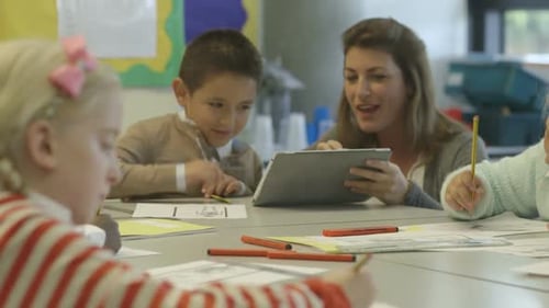Teacher Helping Elementary School Students With Tablet