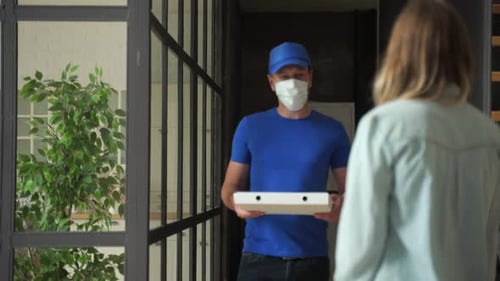 Friendly Pizza Delivery Guy in Protective Medical Mask Handing Order To Customer at Home