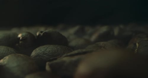 Nahaufnahme des Röstens von Kaffeebohnen, gefilmt in einer dunklen Tonart, der Rauch, der vom Rösten von