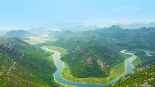 Blue Crnojevica River Flowing Curves Through Green Valley Toward Distant Mountains of Lake Skadar in