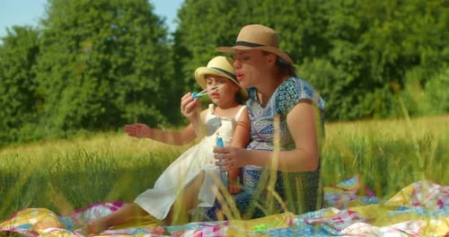 Mother and Daughter Blow Soap Bubbles in the Park