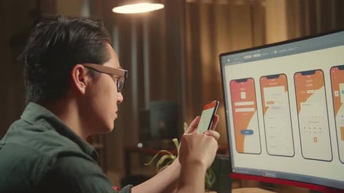 Asian Male Mobile Application Developer Works And Using Mobile Phone With Graphics Computer