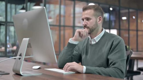 Junger Mann denkt während der Arbeit am Computer