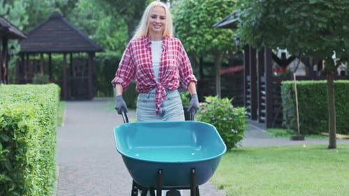 Caucasian Woman Walking in Garden with Blue Wheelbarrow at Daytime
