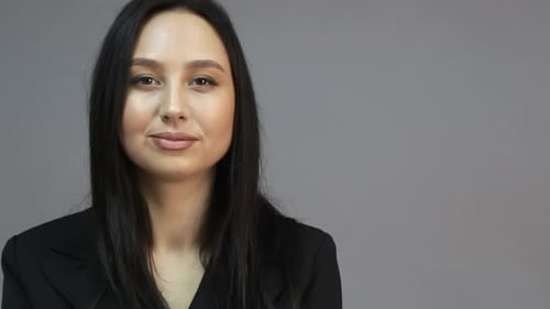Brunette european woman looking at camera while standing in the office on gray background