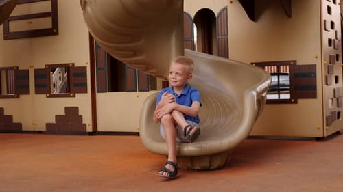 A Small Boy is Sitting on a Slide on the Playground in the Courtyard